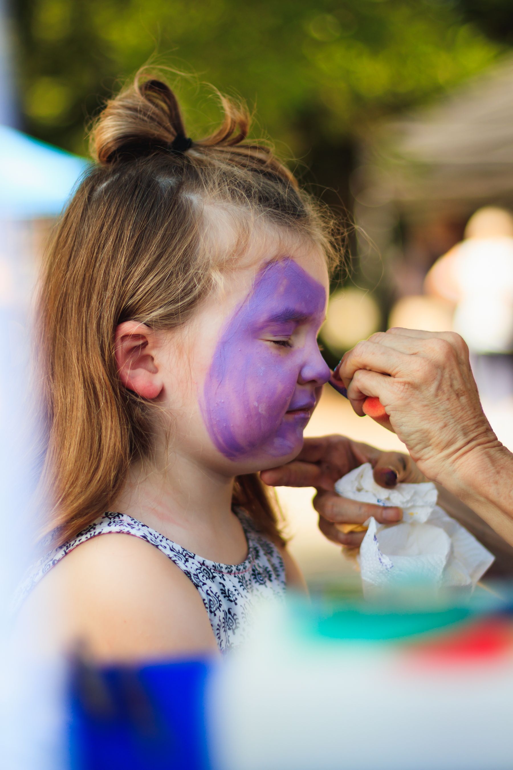 A child having their face painted at an outdoor event.