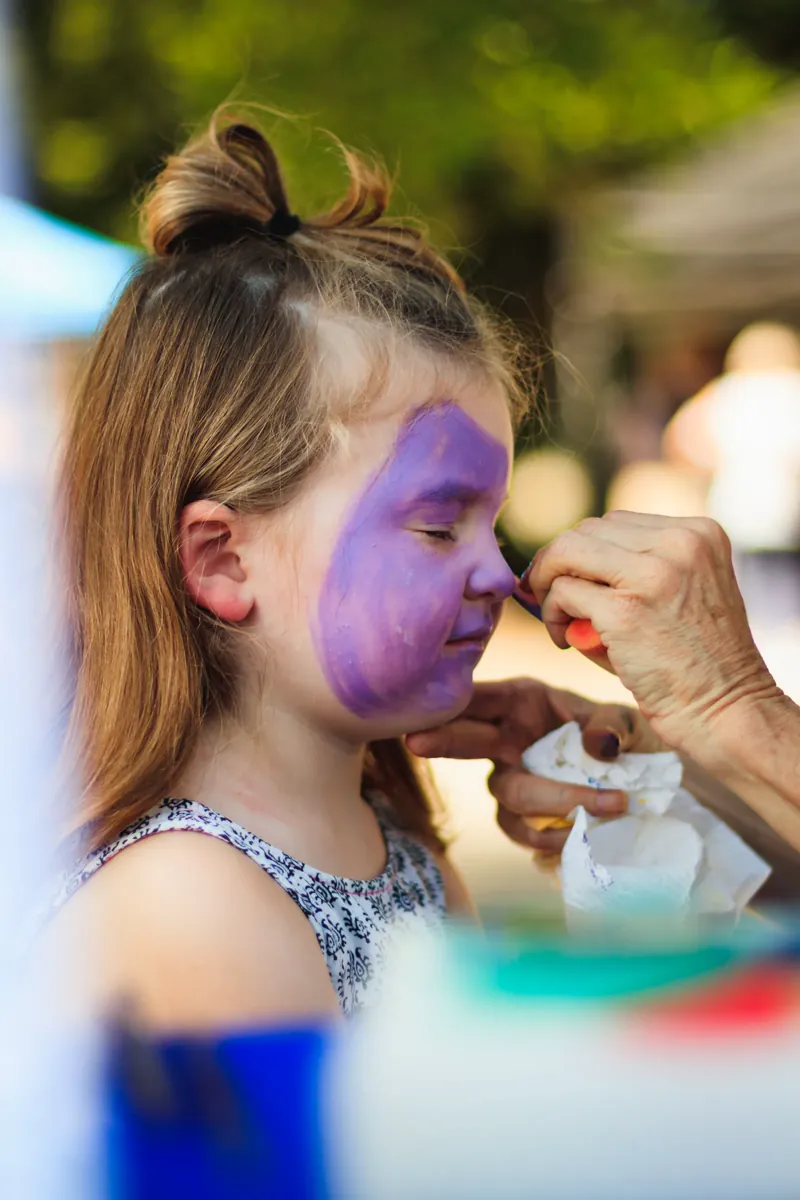 A child having their face painted at an outdoor event.