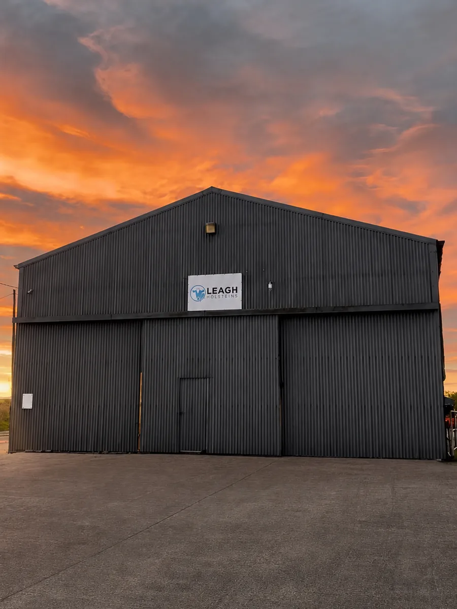 The Leagh Holsteins farm shed at sunset, with an orange sky over the yard.